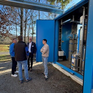 Unternehmer und Forschende unterhalten sich an der Forsthochschule Rottenburg vor dem blauen Container. In diesem befindet sich die Wasserstoffanlage.