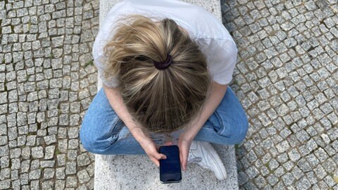 Typische Haltung in heutiger Zeit: mit gesenktem Kopf auf das Handy schauen
