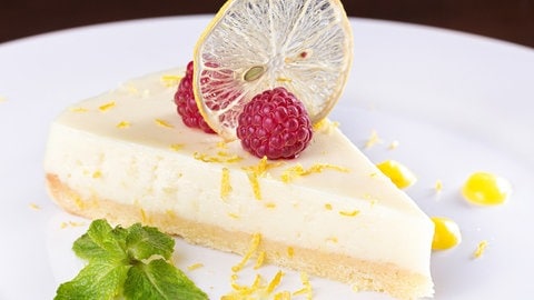 Rezept Zitronentarte mit Himbeeren: Ein Stück Zitronentarte liegt auf einem weißen Teller, garniert mit Minzeblättern