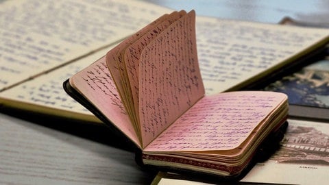 Dicht beschriebenes Tagebuch liegt auf einem Fotoalbum: Erinnerungen festhalten, Bedrückendes loswerden oder einfach Spaß am Schreiben – es gibt viele Gründe, weshalb Menschen Tagebuch schreiben. In der Poesietherapie wird es genutzt, um Probleme und sogar Traumata aufzuarbeiten. (Aufgenommen im Deutschen Tagebucharchiv)