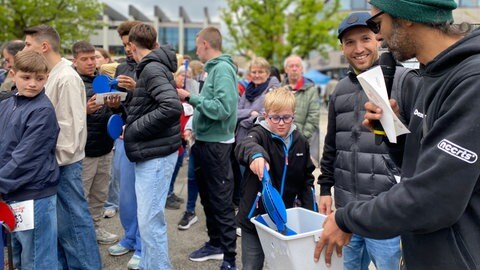 Ein Junge greift in eine Kiste und holt einen Tischtennisschläger heraus. Er macht beim Weltrekordversuch im "Mäxle"-Tischtennisspiel in Reutlingen mit. 