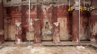 Antike Fresken des Dionysos-Kults in einer römischen Villa in Pompeji. Rötliche Wandmalereien zwischen teilweise erhaltenen Säulen zeigen Einweihungsrituale der dionysischen Mysterien.