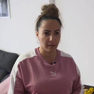 Alleinerziehende Frau sitzt im Zimmer vor weißer Wand