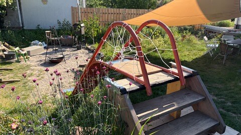 Eine große Rutsche führt hinunter in den etwas tieferliegenden Bereich, in dem ein großer Grill steht.