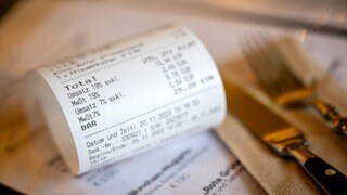 Eine Rechnung mit Umsatzsteuer und Mehrwertsteuer liegt auf der Speisekarte eines Restaurants. Durch die Abschaffung der Bonpflicht könnte Steuerhinterziehung in der Gastronomie leichter werden.
