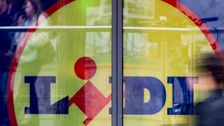 Eine Person läuft, unscharf dargestellt, an einem Schaufenster mit riesigem Lidl-Logo dahinter vorbei. (Symbolbild) Nachdem Lidl vor dem Landgericht Heilbronn erneut eine Niederlage einstecken musste, will das Unternehmen mit Sitz in Bad Wimpfen (Kreis Heilbronn) in Berufung gehen. Es geht um Irreführung bei Preisen im Prospekt.