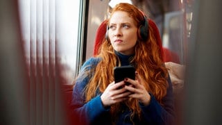 Eine Frau mit Kopfhörern während einer Bahnfahrt 