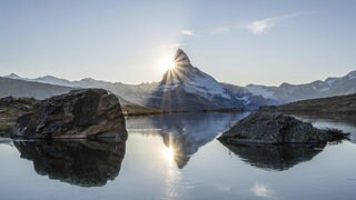Matterhorn und Spiegelung im Stellisee bei Sonnenuntergang. Die Sonne geht hinter dem Berg unter. 
