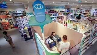Eine Mitarbeiterin führt in einer dm-Filiale ein Augenscreening bei einem Kunden durch.