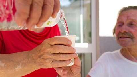 Älterer Mann mit Wasserbecher. Hitze ist eine Gefahr für die Gesundheit - besonders ältere Menschen sind durch Hitzewellen gefährdet.