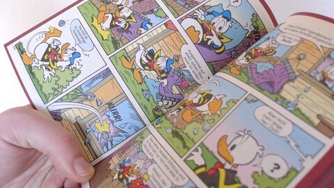 Ein "Lustiges Taschenbuch" mit Donald Duck Zeichnungen liegt aufgeschlagen in einer Hand.