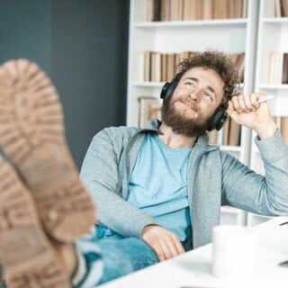 Junger Mann hat entspannt die Schuhe auf den Schreibtisch gelegt: Im Job kommen echte Pausen oft zu kurz. Dabei zeigt die Hirnforschung: Unser Gehirn braucht das Nichtstun.
