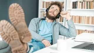 Junger Mann hat entspannt die Schuhe auf den Schreibtisch gelegt: Im Job kommen echte Pausen oft zu kurz. Dabei zeigt die Hirnforschung: Unser Gehirn braucht das Nichtstun.