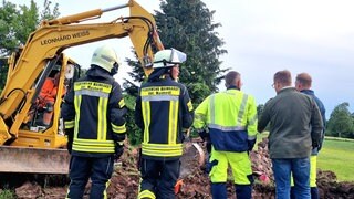 Einsatzkräfte der Feuerwehr stehen vor dem Bagger an der Stelle, wo das Gas in Mainhardt ausgetreten ist. Bauarbeiter hatten damit die B14 lahm gelegt.