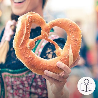 Eine Frau hält eine Brezel. Die Frau lächelt. Sie hat ein Dirndl an. Ein Dirndl ist ein traditionelles Kleid aus Deutschland. Rechts das SWR Logo für Leichte Sprache.