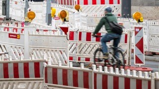 Symbolbild | Ein Fahrradfahrer fährt über eine Strasse, die mit Warnbaken vollgestellt ist.