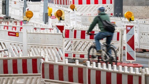 Symbolbild | Ein Fahrradfahrer fährt über eine Strasse, die mit Warnbaken vollgestellt ist.