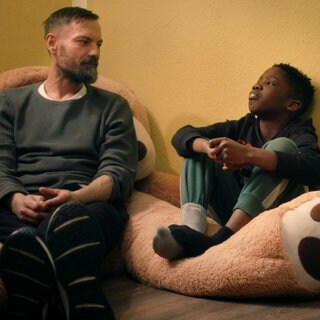 Ein Mann und ein Junge sitzen nebeneinander auf einem großen Teddybären
