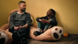 Ein Mann und ein Junge sitzen nebeneinander auf einem großen Teddybären