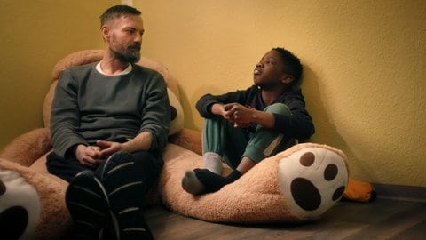 Ein Mann und ein Junge sitzen nebeneinander auf einem großen Teddybären