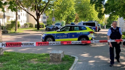 Polizisten und Anwohner hinter einem Absperrband in einem Wohnviertel