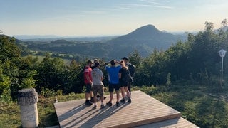 Die Wandergruppe Wandersocken steht auf einer Aussichtsplattform und schaut in die Ferne. Beim gemeinsamen Wandern werden aus Fremden oft Freunde.