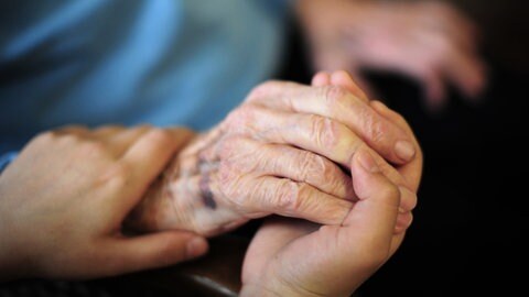Eine junge Frau hält die Hand einer alten Dame: Heute ermöglichen rund 55.000 ehrenamtliche Helferinnen und Helfer eine ambulante Sterbebegleitung zu Hause. Doch junge Freiwillige, die sich engagieren wollen, fehlen.