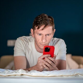 Ein Mann benutzt sein Smartphone auf dem Bett liegend