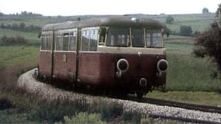 Eine Eisenbahn fährt auf Schienen in einer grünen Landschaft