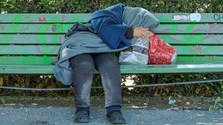 Eine Obdachlose schläft auf einer Bank.