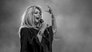 Nachruf zum Tod von Bonnie Tyler: Sie singt während eines Konzerts im Jahr 2021. Sie trägt ein weites schulterfreies Kleid,  in der rechten Hand das Mikro.
