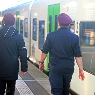Zwei Zugblegiter laufen im Dienst einen Bahnsteig entlang. Das Land möchte in einem Pilotprojekt Doppelbesetzungen in den Zügen testen. 