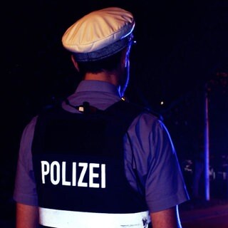 Ein Polizist steht im Dunkeln vor einem Polizeiauto.