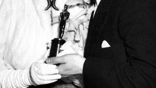 Eine junge Judy Garland hält eine Oscar Statue in der Hand und bekommen von einem jungen Mann einen Kuss auf die Backe