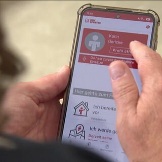 Eine Frau hält ein Handy in der Hand und nutzt die DRK-App