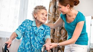 Eine junge Pflegekraft unterstützt eine alte Frau in deren Wohnung.