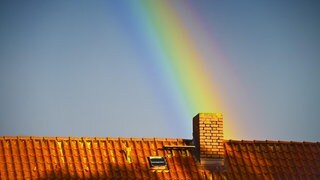 Ein Regenbogen trifft auf einem Hausdach auf einen Schornstein. Die Wärmewende betrifft viele Menschen in Baden-Württemberg. (Symbolbild)