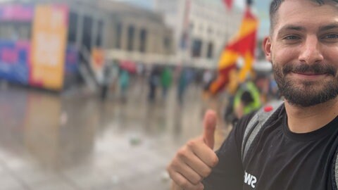 Loris Hoffmann lächelt bei regnerischem Wetter am Ende des CSD Stuttgart 2025 mit erhobenem Daumen in die Kamera.