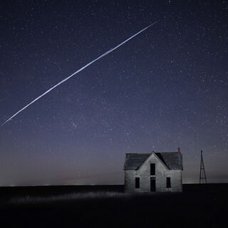 Auf diesem Foto, das am 6. Mai 2021 mit Langzeitbelichtung aufgenommen wurde, fliegt eine Reihe von Starlink-Satelliten über ein altes Steinhaus in der Nähe von Florence, Kansas