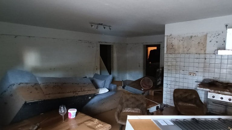 In einer Kellerwohnung liegen kaputte Gegenstände und Möbelstücke wild verstreut. Auf dem Boden ist schlammiges Wasser.