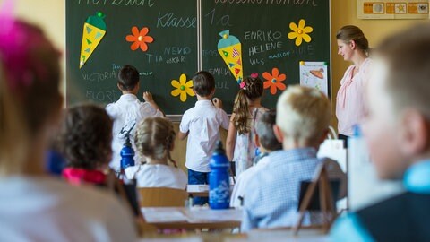 Schüler im Klassenzimmer vor einer Schultafel, auf die sie ihre Namen schreiben. 