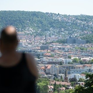 Ein Mann sitzt auf einer Bank im Schatten und blickt auf Stuttgart (Archivbild).