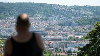 Ein Mann sitzt auf einer Bank im Schatten und blickt auf Stuttgart (Archivbild).