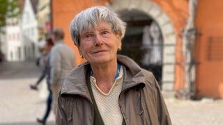 Alte Dame mit weißen Haaren und brauner Jacke.