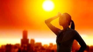 Eine Frau schützt in heißer Sonne ihre Augen: Hitzewellen sind belastend, doch mit der richtigen Anpassung lassen sie sich gut überstehen. Dazu gehört, sich nicht nur in klimatisierten Räumen zu schonen, sondern den Körper an Hitze zu gewöhnen.