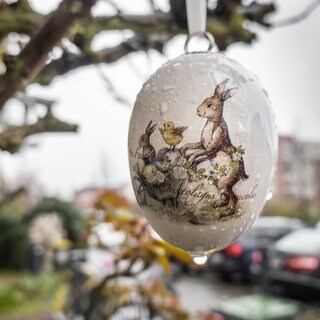 Ein mit einem Hasenmotiv bedrucktes Porzellan-Osterei hängt im Regen vor einem Hauseingang.