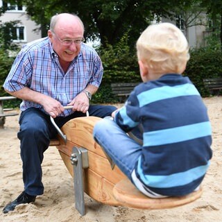 Ein "Leih-Opa" wippt mit einem dreijährigen Jungen auf dem Spielplatz.
