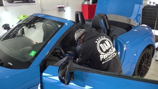 Ein Mitarbeiter von Daniel Kampmann reinigt ein blaues Auto in der Werkstatt.