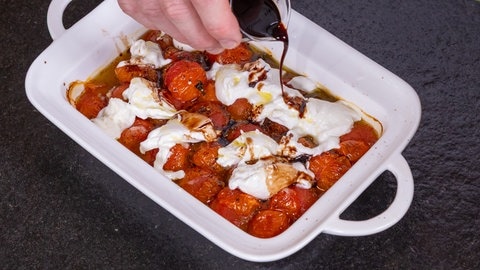 Ofengericht mit Tomaten, Burrata und Basilikum: Die gebackenen Tomaten in der Auflaufform mit bereits hinzugefügten Burrata werden mit Balsamicoessig übergossen.