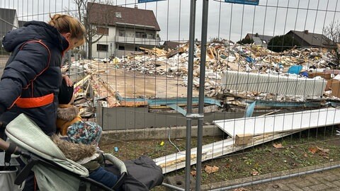 Eine Familie steht vor einem Bauzaun in Durmersheim. Die Kita liegt nach einem Brand in Trümmern.